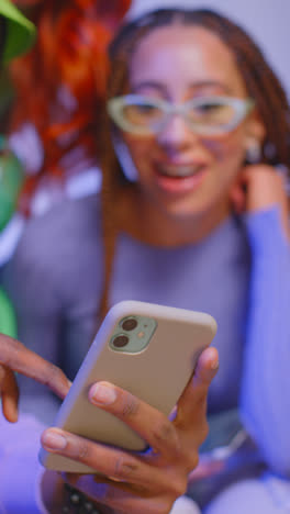 Close-Up-Vertical-Video-Studio-Shot-Of-Young-Gen-Z-Friends-Sitting-On-Sofa-Sharing-Social-Media-Post-On-Mobile-Phones